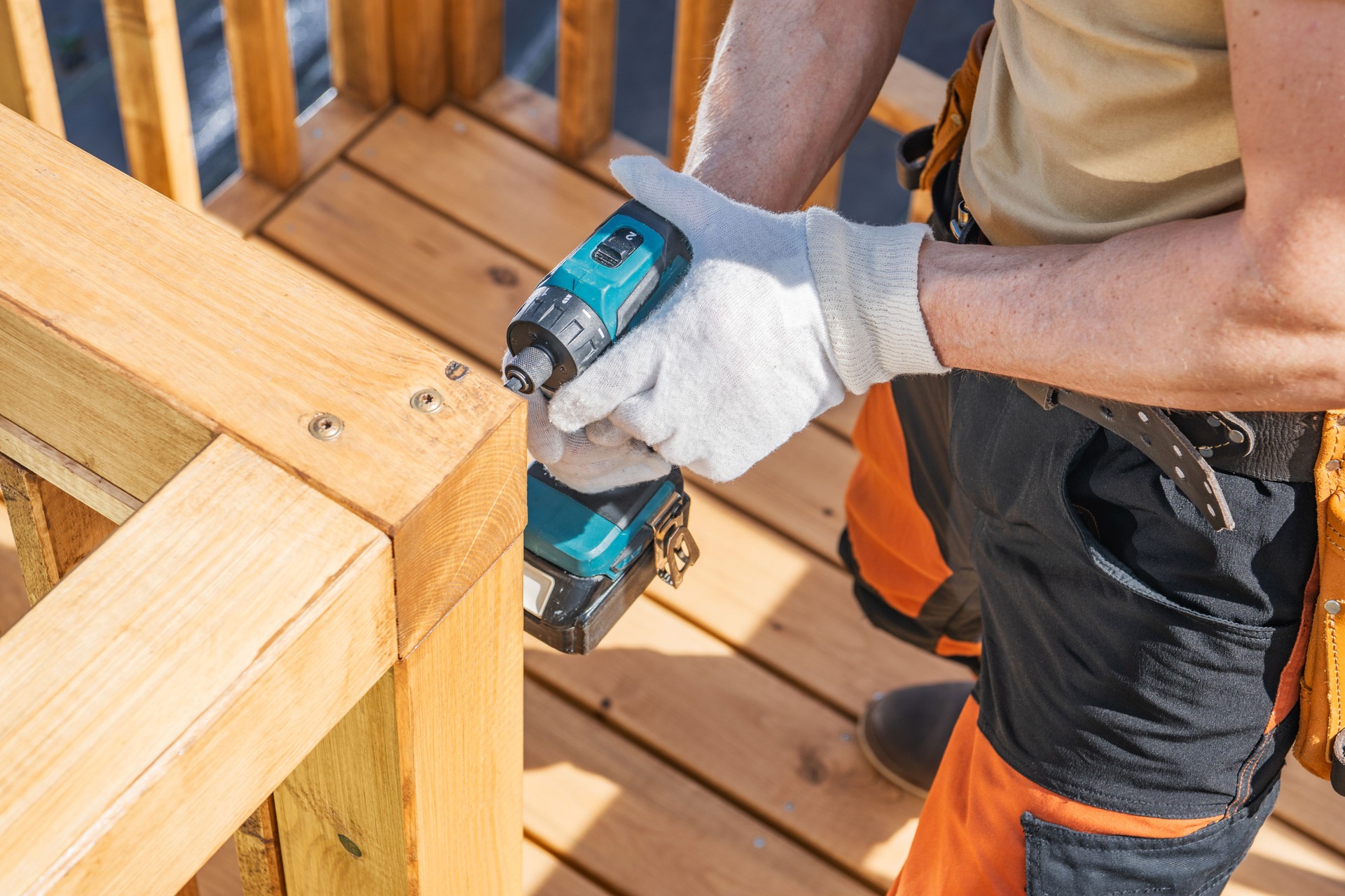Person Using a Cordless Drill to Secure Wooden Railing on a Sunny Day at a Construction Site